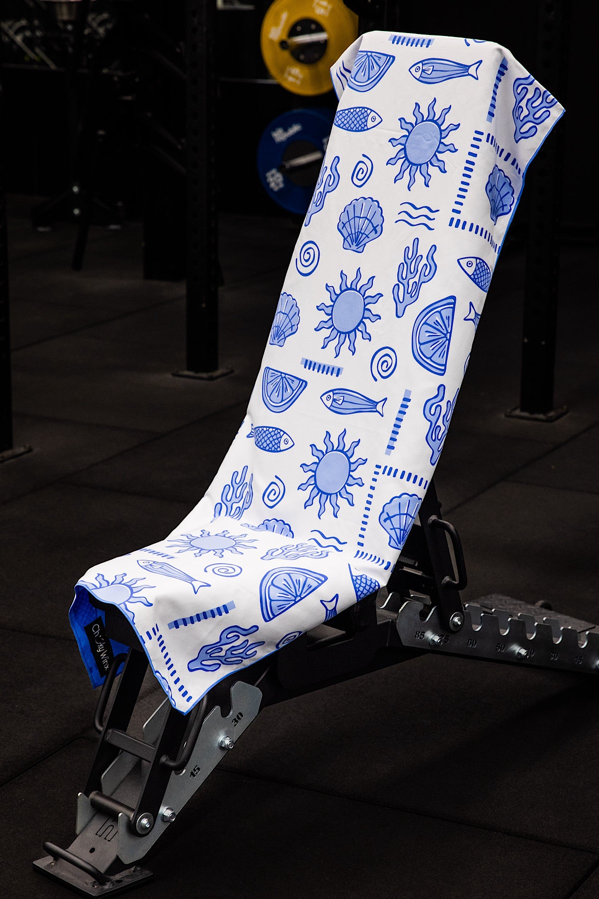 White towel with blue ocean-themed patterns draped over a black gym bench.